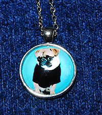 Pug Necklace 2 - Round pendant with fawn Pug on aqua background dressed in a black tee shirt.